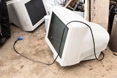 Zużyte monitory leżące na ziemi na wysypisku elektrośmieci; jeden z monitorów ma widoczny kabel .