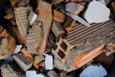 A pile of broken fragments of construction waste, including pieces of red clay blocks with visible voids and white pieces of polystyrene foam.